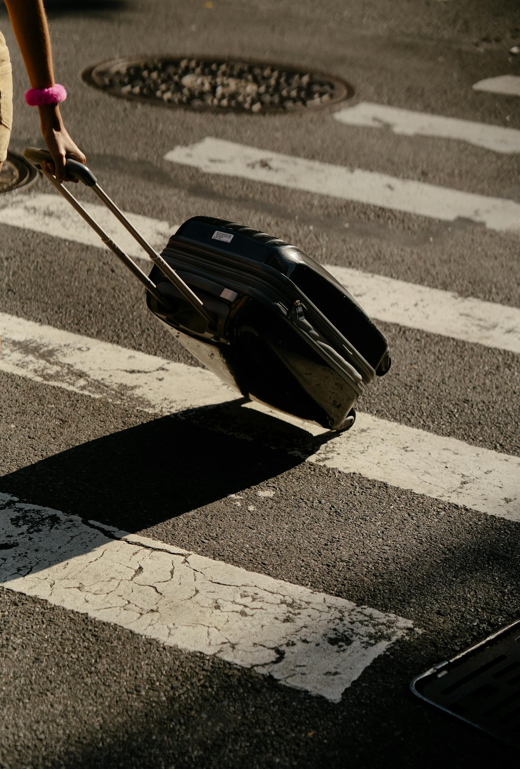 Close-up of a Person Walking with a Suitcase on a Street Crossing